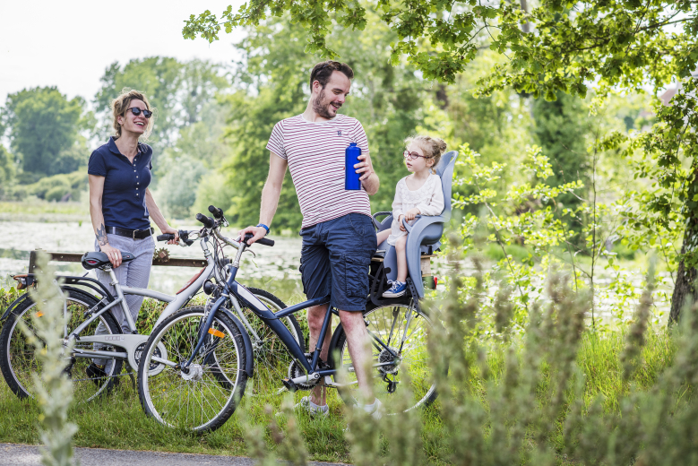 couple avec enfant à vélo au bord d'un étang